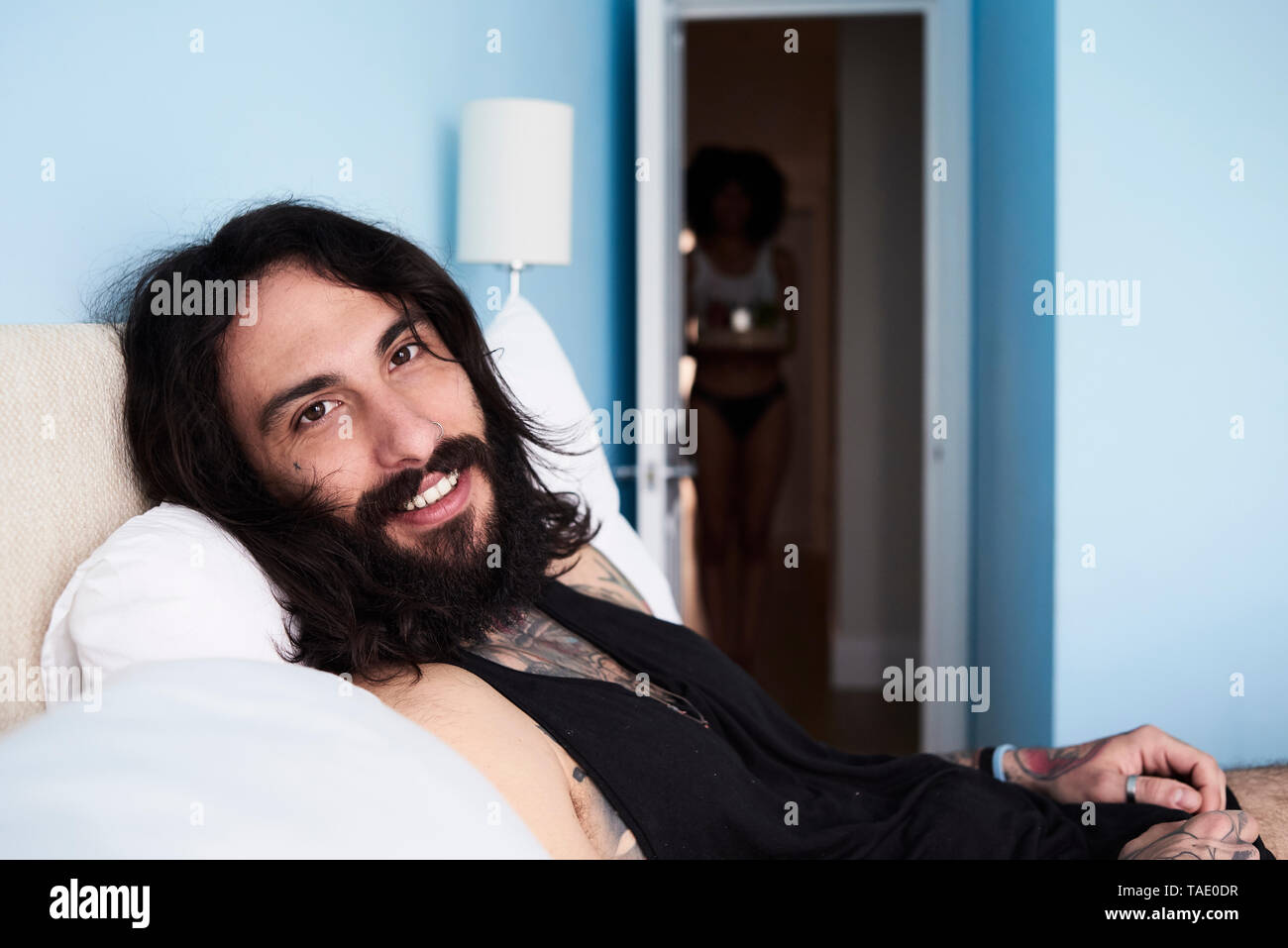 Ritratto di sorridere tatuato uomo disteso n letto con la fidanzata in background Foto Stock