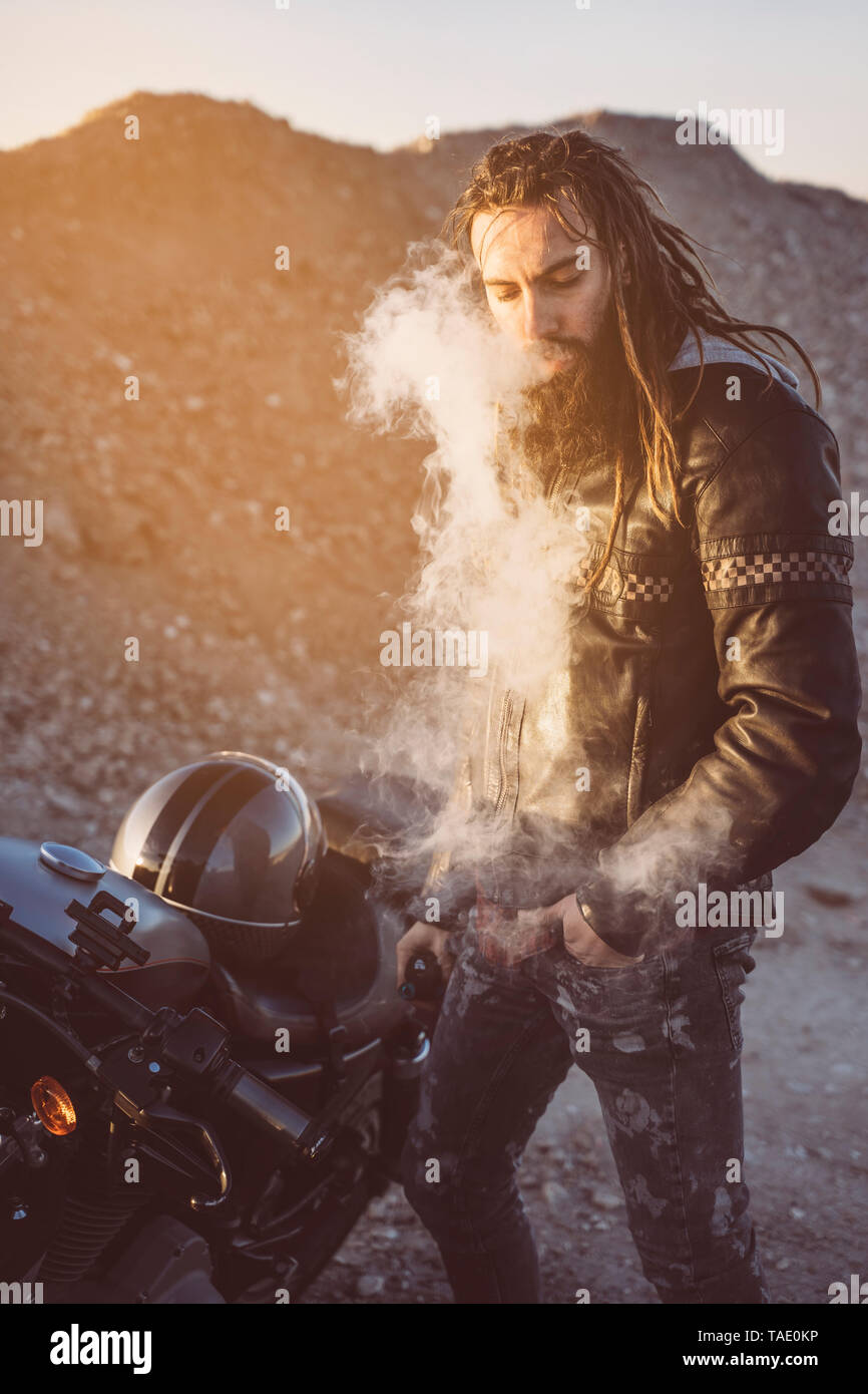 Ritratto di barbuto biker con dreadlocks di fumare sigaretta elettronica Foto Stock