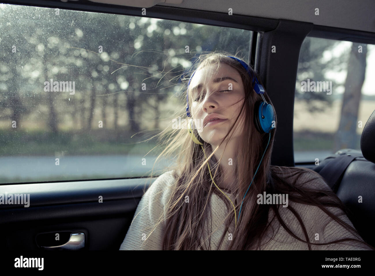 Giovane donna con capelli spazzate dal vento in un auto che indossano le cuffie Foto Stock