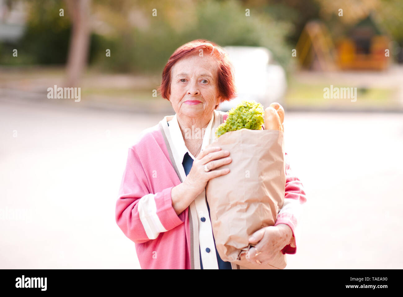 Sorridente donna senior 70-80 anno vecchia azienda sacchetto di carta con cibo fresco all'esterno. Guardando alla fotocamera. Foto Stock
