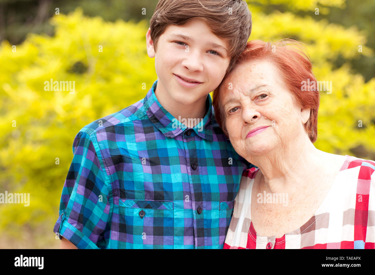 Sorridente donna anziana con teen boy all'esterno. Guardando alla fotocamera. La famiglia felice. Foto Stock