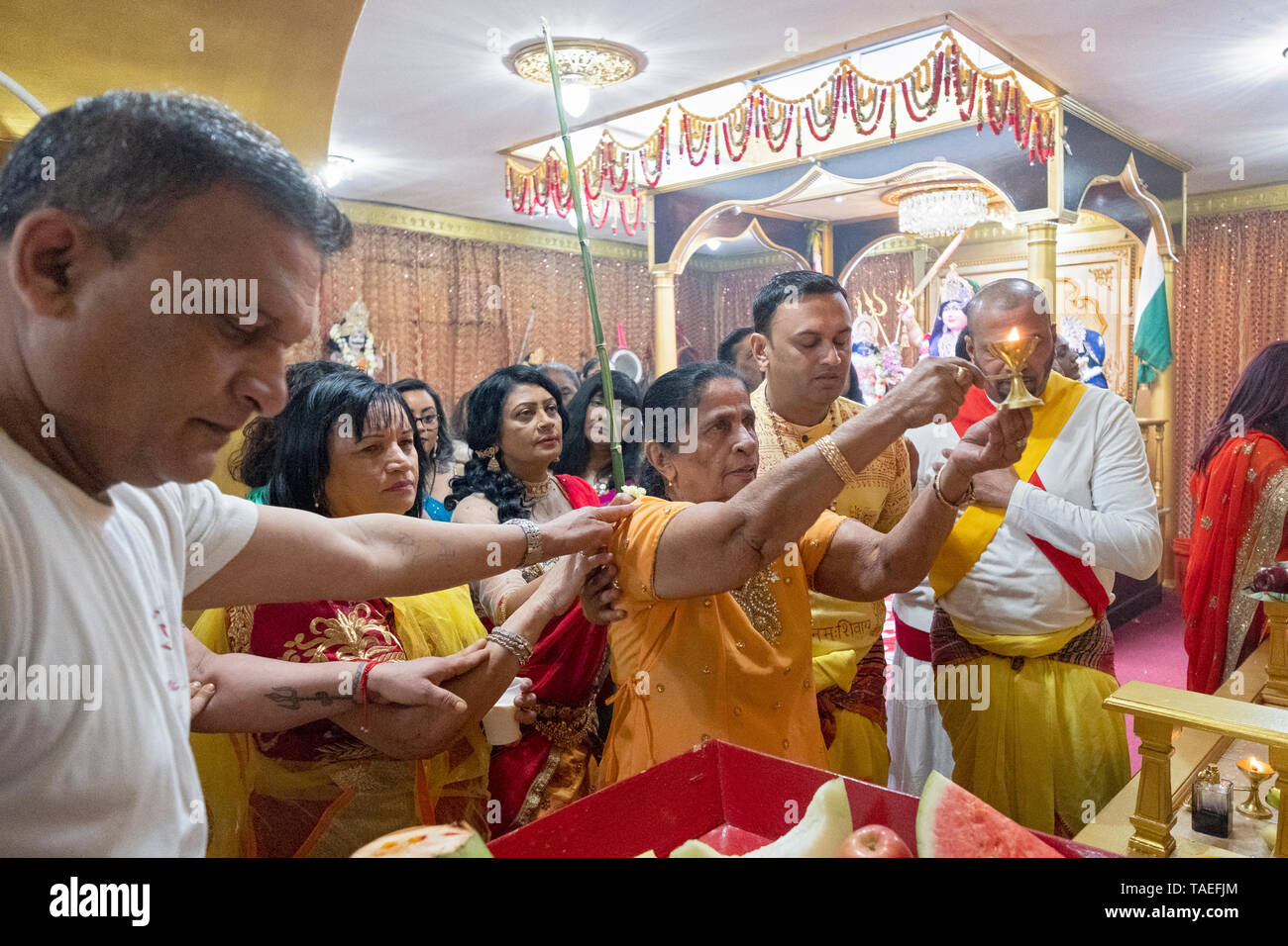 Circondato dalla famiglia, una donna indù nel suo fine anni settanta offre il fuoco per le divinità come un atto di apprezzamento. In Ozone Park, Queens, NYC. Foto Stock
