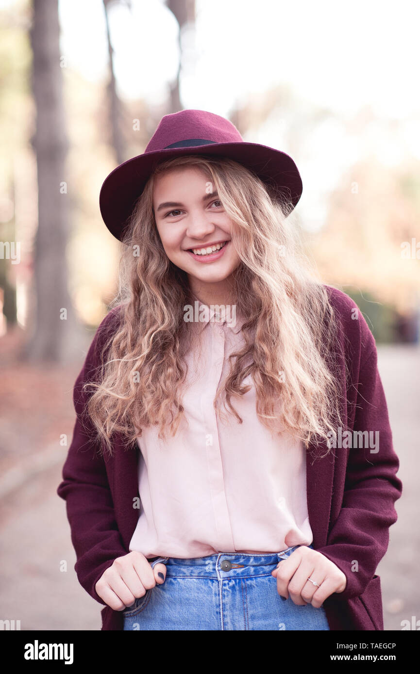 Autunno ritratto della bionda sorridente ragazza adolescente 14-16 anni elegante da indossare giacca invernale e il feltro di hat all'esterno. Guardando alla fotocamera. Buon umore. Posit Foto Stock