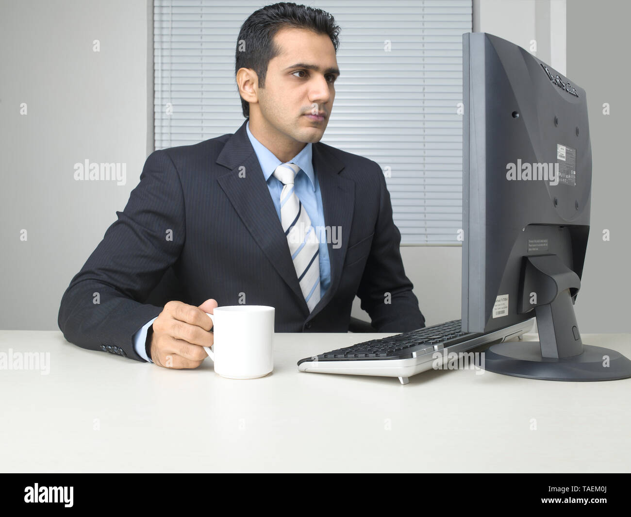 CORPORATE EXECUTIVE bere il tè/caffè mentre si lavora alla propria scrivania Foto Stock