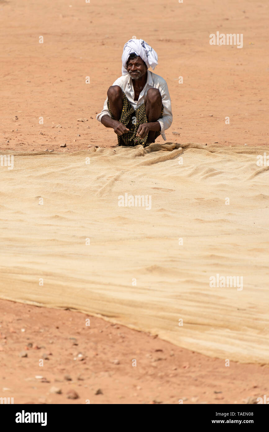 Ritratto verticale di un anziano pescatore riassettavano le reti in India. Foto Stock