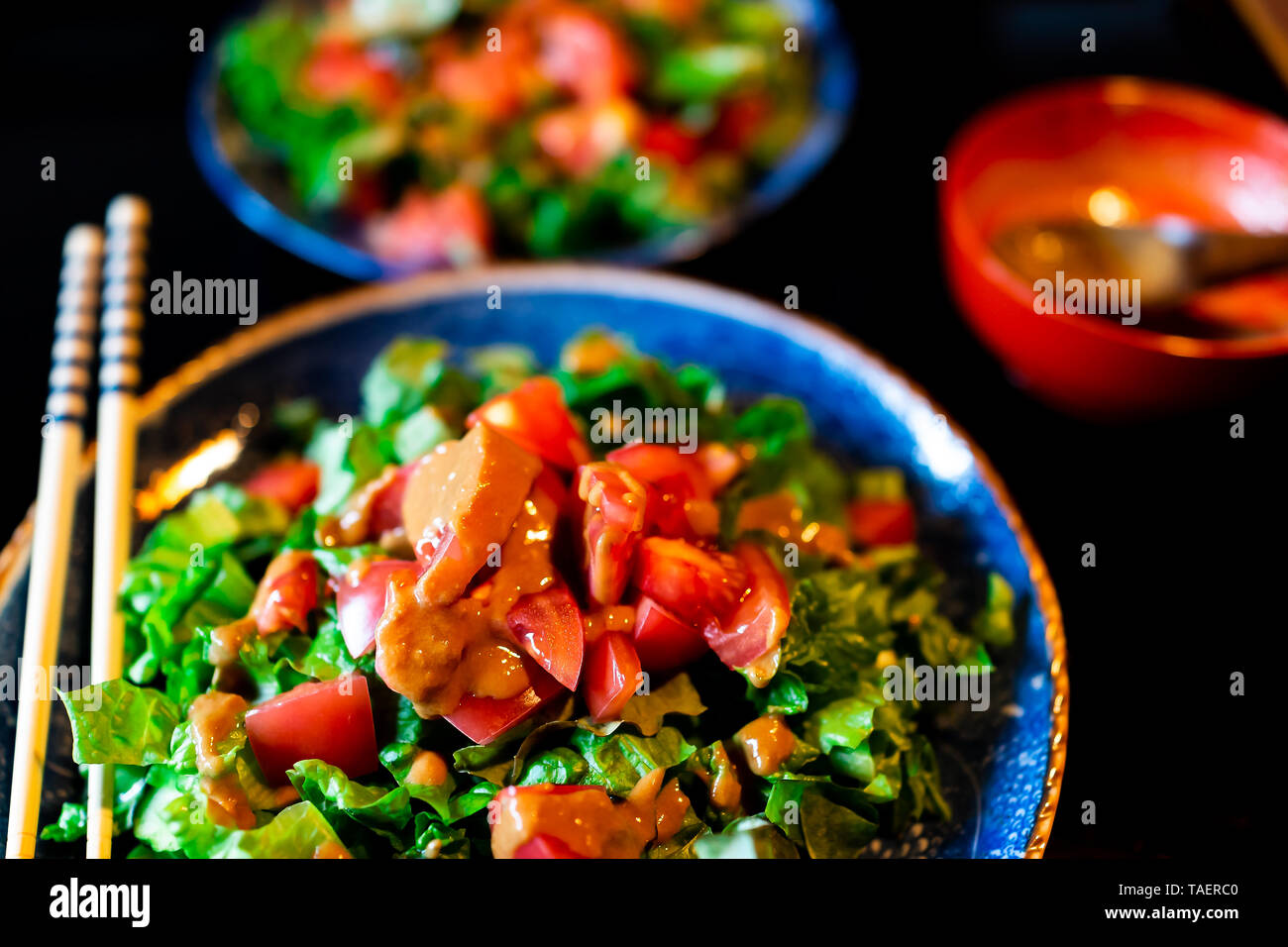 Tradizionale ryokan giapponese ristorante con nero laccato tavolo in legno e piatto di insalata closeup con dressing e bastoncini Foto Stock