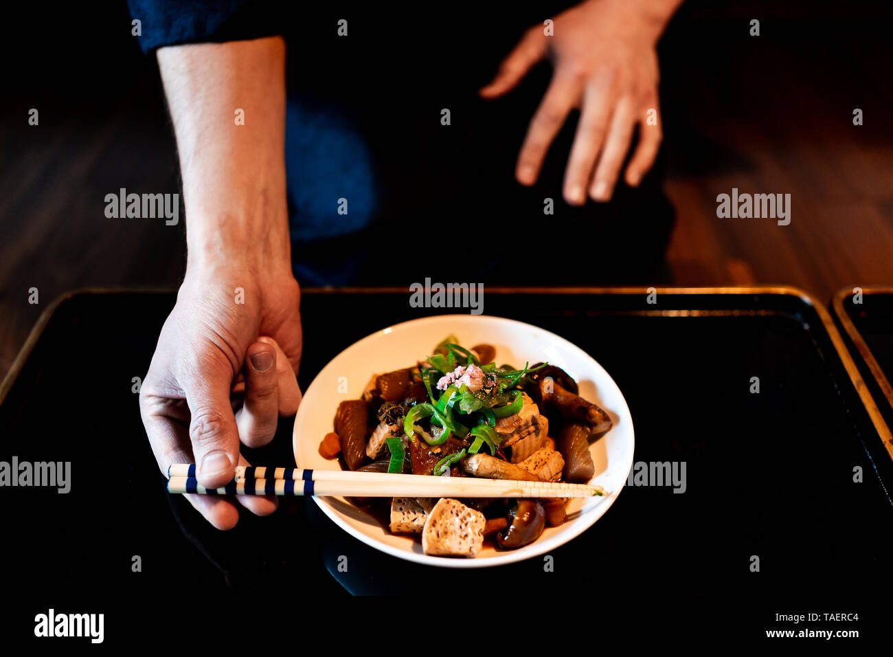 Casa tradizionale giapponese o ryokan ristorante con nero laccato tavolo in legno e piatto closeup con uomo in kimono o yukata prelievo di bacchette Foto Stock