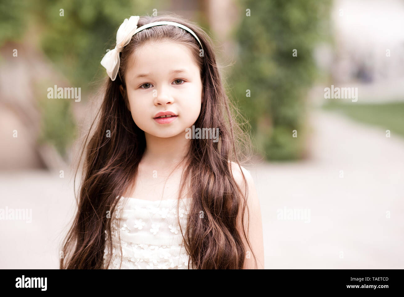 Bella ragazza di capretto 4-5 anno vecchio con capelli lunghi che indossa la fascia di prua all'aperto vicino. Guardando alla fotocamera. Infanzia. Foto Stock