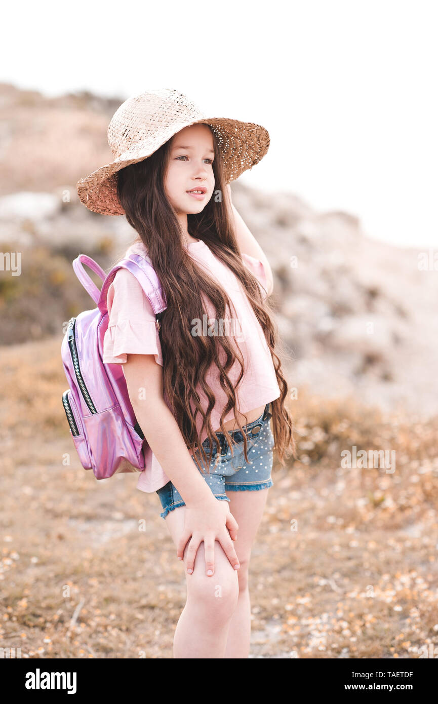 Carino kid girl 4-5 anno indossando cappello di paglia e zaino rosa all'esterno. Guardando in avanti. Durante la stagione estiva. Foto Stock