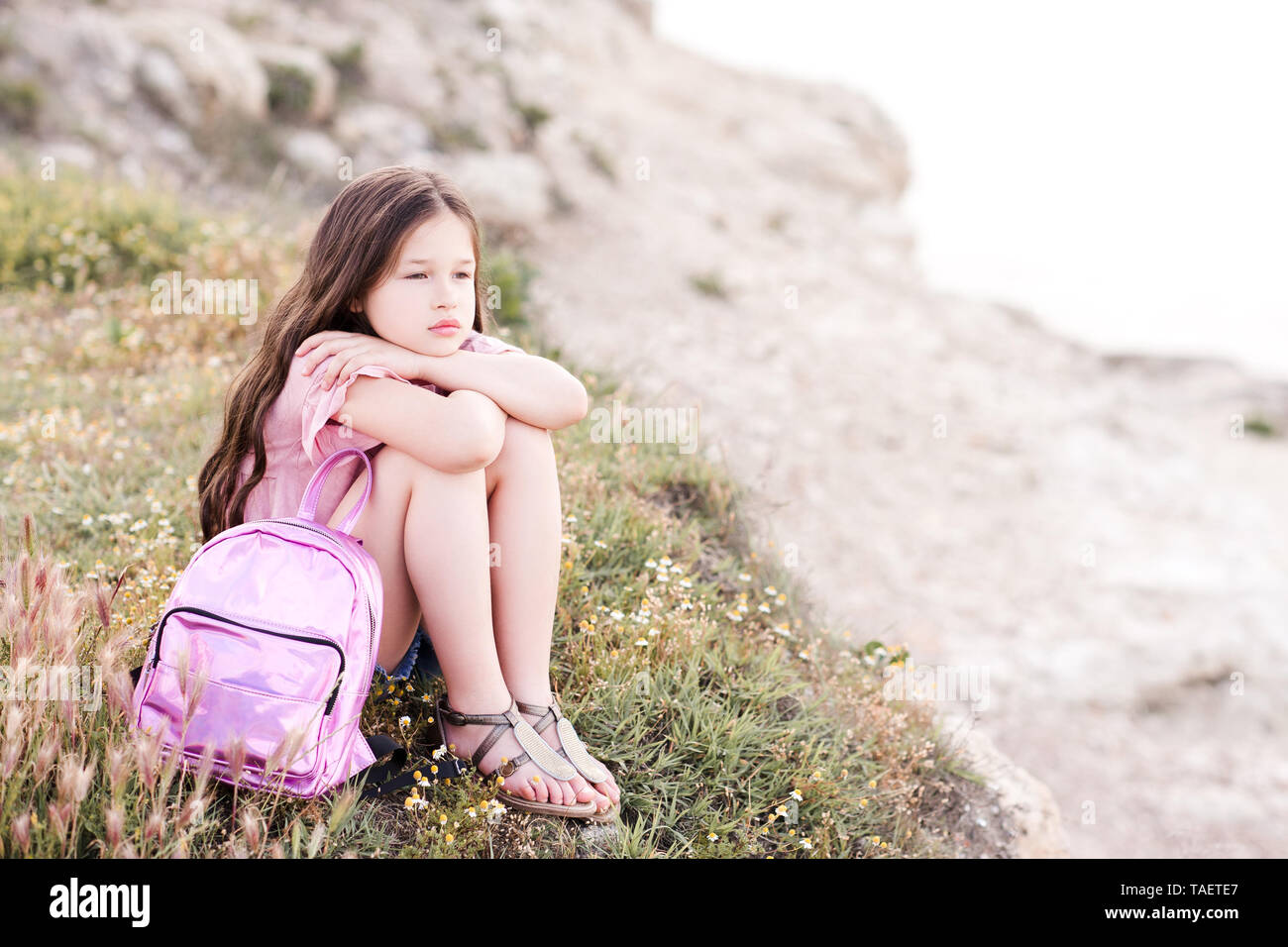 Carino kid girl 4-5 anno vecchio in appoggio sulla parte superiore della roccia all'esterno. Guardando in avanti. Infanzia. Foto Stock