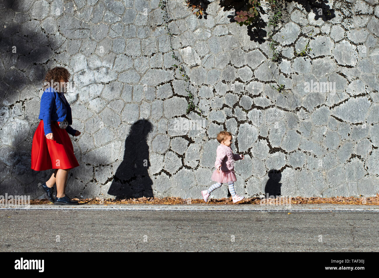 Bambina in esecuzione con la sua madre ad un muro di pietra Foto Stock