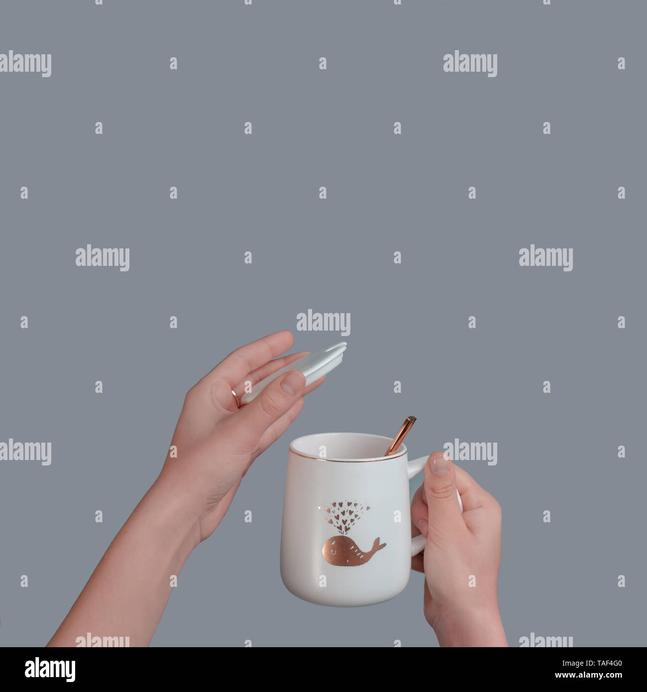 Tazza bianca con un cucchiaio in mano di un adolescente, isolato su un sfondo grigio. Foto Stock