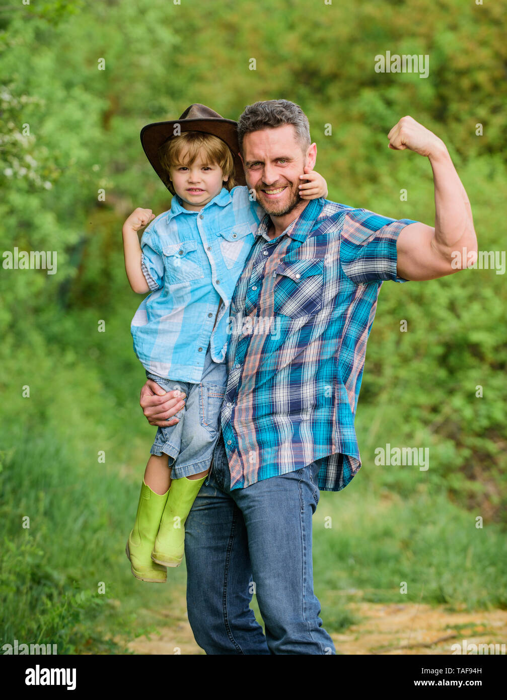 Forte il padre e il figlio nel cappello da cowboy sul ranch. kid in stivali  di gomma. uomo felice papà nella foresta. natura e uomo. il giorno della  famiglia. felice giornata della