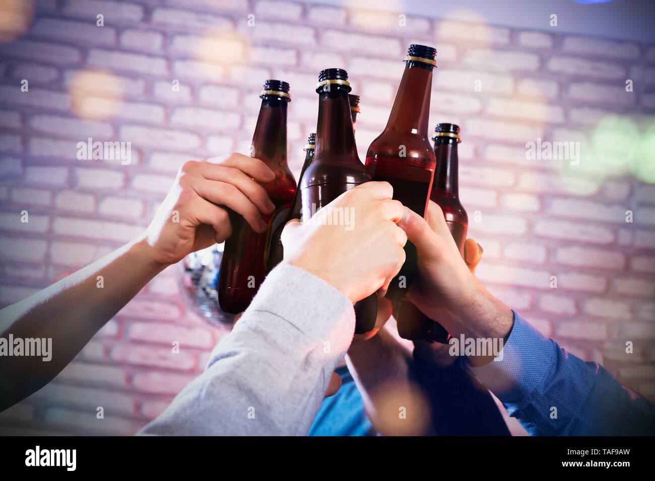 Close-up di un amico con le mani in mano la tostatura le bottiglie di birra presso il Bar contro un muro di mattoni Foto Stock