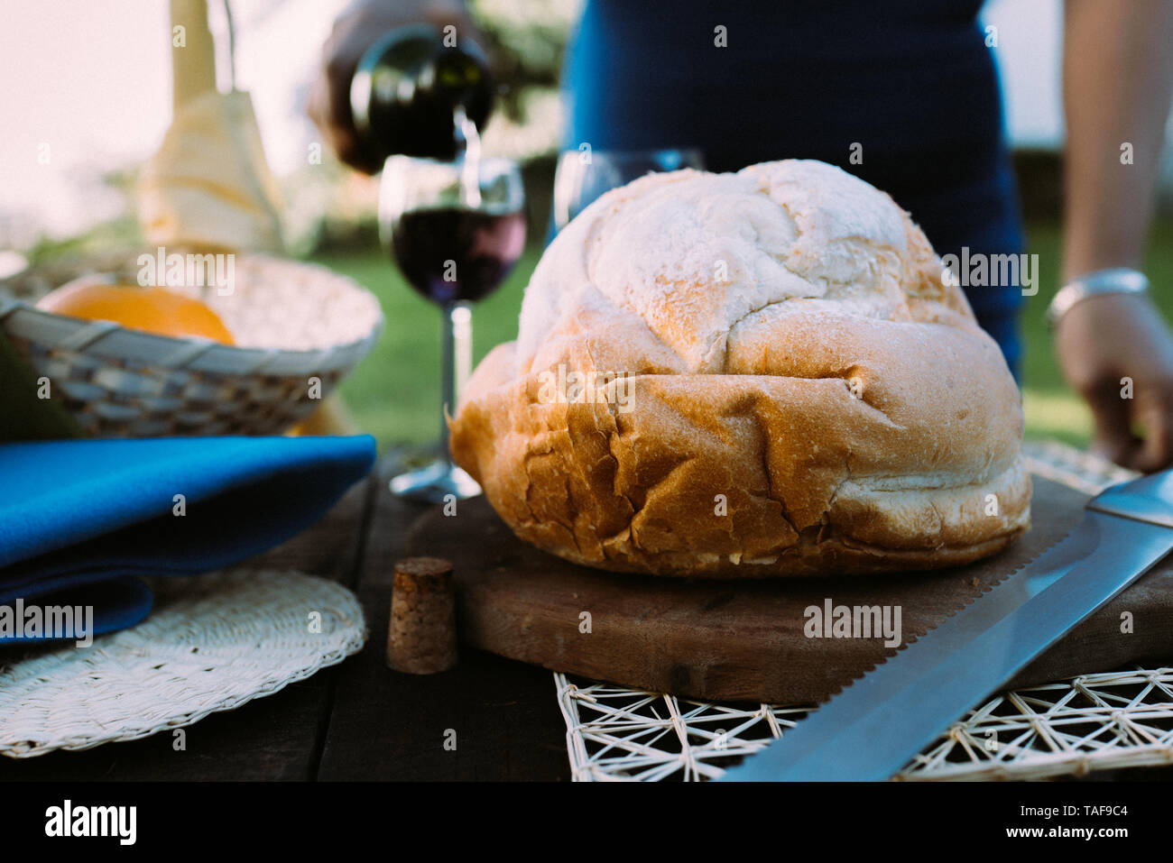 Donna che serve vino rosso in un bicchiere di vetro, con un pane focalizzata sul primo piano in un ambiente intimo e romantico celebrazione Foto Stock