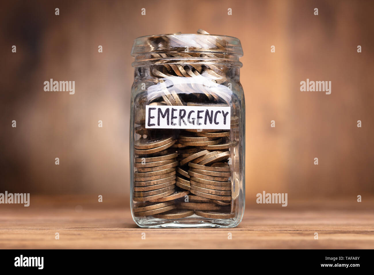 Monete in vaso con etichetta di emergenza sulla scrivania in legno Foto Stock
