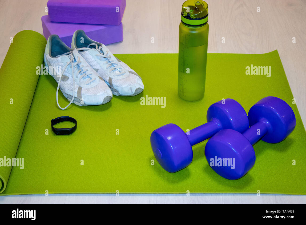 Fintes manubri, sneakers, una bottiglia di acqua minerale e un braccialetto di fitness su un tappeto verde, sport concetto, la foto in orizzontale Foto Stock