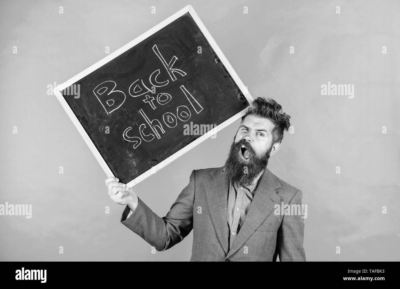 Insegnante uomo barbuto detiene blackboard con iscrizione torna a scuola sfondo verde. Continuare a lavorare. Insegnante con capelli tousled stressante circa anno scolastico inizio. Insegnamento occupazione stressante. Foto Stock