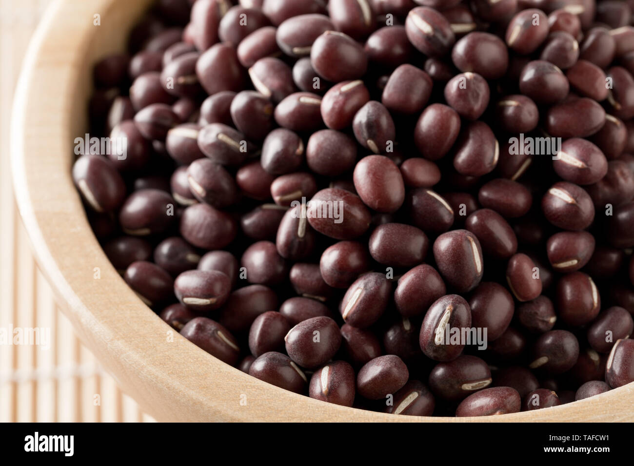 Materie, non cotte, essiccato adzuki (rosso) Mung bean in ciotola di legno su sfondo di bambù con tappetino di messa a fuoco selettiva Foto Stock