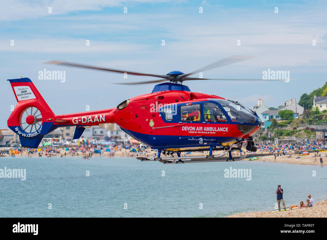 Lyme Regis, Dorset, Regno Unito. 25 maggio 2019. Devon Air Ambulance elicottero atterra sulla spiaggia affollata a Lyme Regis. L'elicottero decolla dall'affollata spiaggia con un paziente a bordo. Credito: Celia McMahon/Alamy Live News. Foto Stock