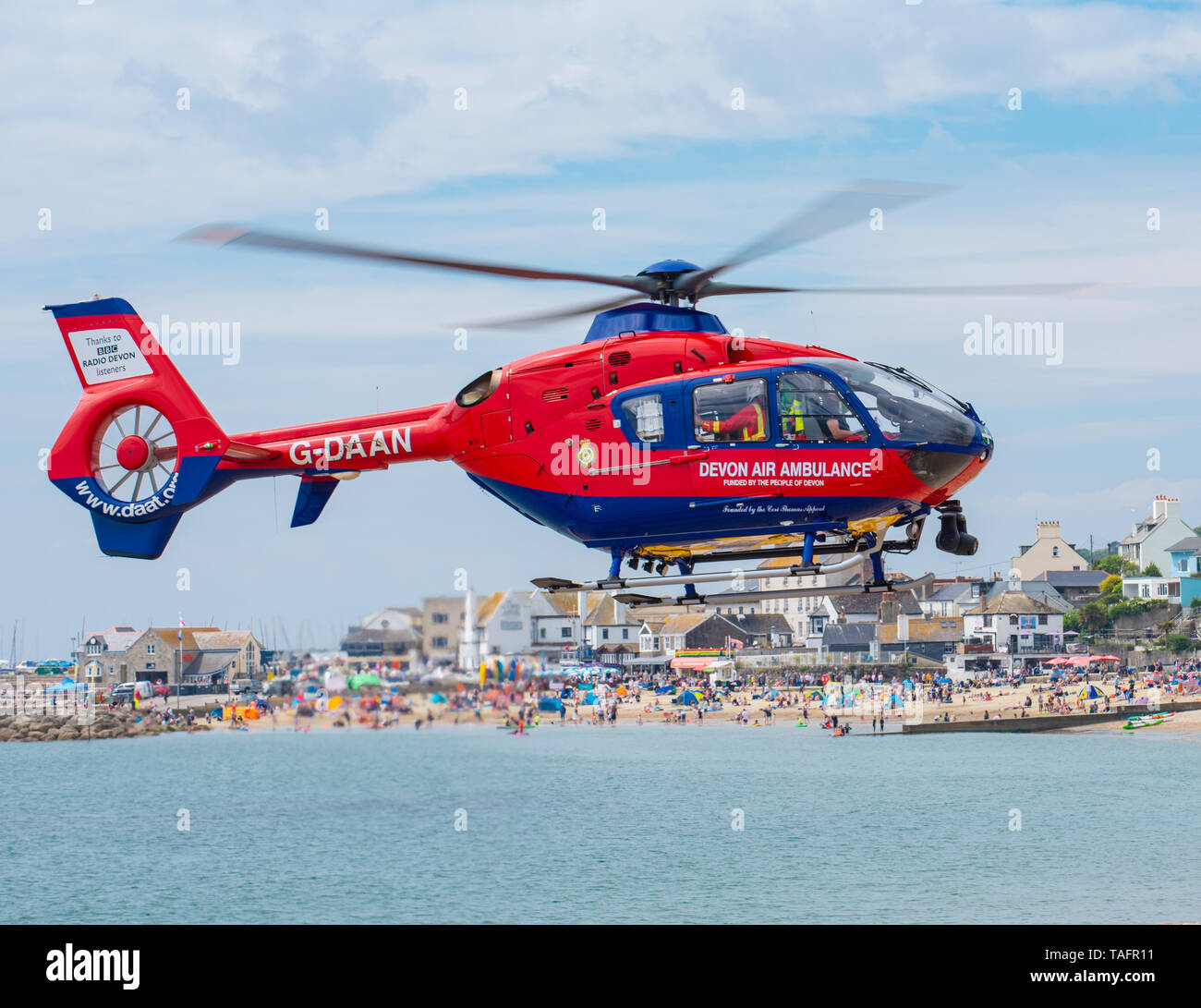 Lyme Regis, Dorset, Regno Unito. 25 maggio 2019. Devon Air Ambulance elicottero atterra sulla spiaggia affollata a Lyme Regis. L'elicottero decolla dall'affollata spiaggia con un paziente a bordo. Credito: Celia McMahon/Alamy Live News. Foto Stock