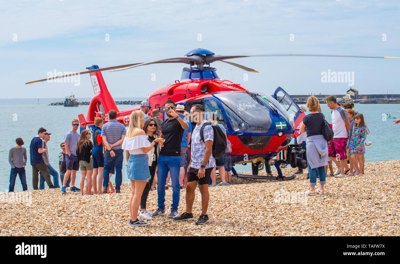 Lyme Regis, Dorset, Regno Unito. 25 maggio 2019. Meteo REGNO UNITO: folle di turisti e visitatori accorrono per la spiaggia di Lyme Regis a crogiolarvi al sole caldo. Il Devon Air Ambulance elicotteri genera interesse tra gli spettatori come si assiste ad una emergenza sulla spiaggia affollata. Credito: Celia McMahon/Alamy Live News. Credito: Celia McMahon/Alamy Live News Foto Stock