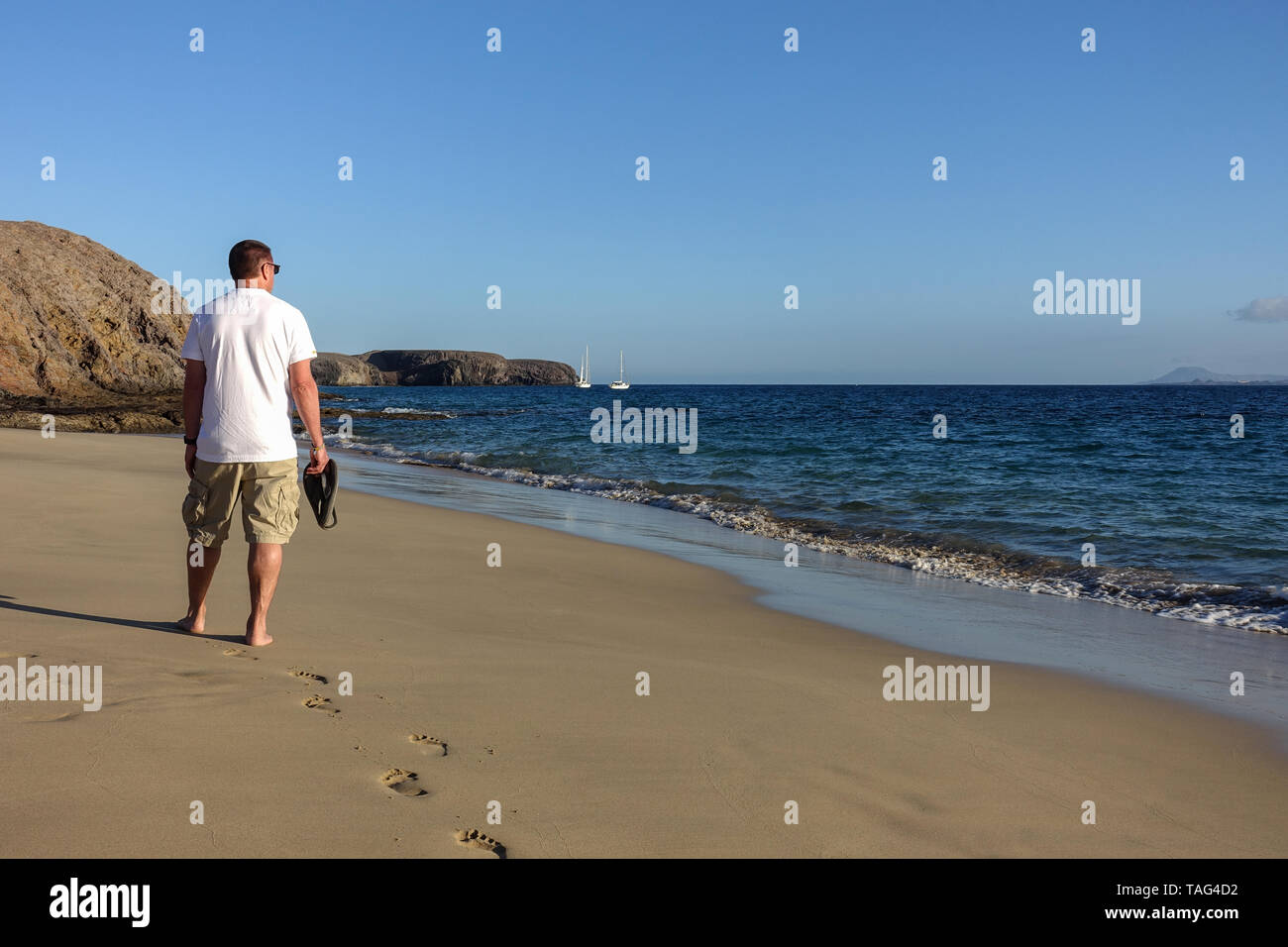 Un uomo adulto passeggiate lungo una tranquilla deserta Spiaggia Papagayo a Lanzarote, catturati nel sole di sera la vista mostra il retro dell'uomo di mezza età Foto Stock