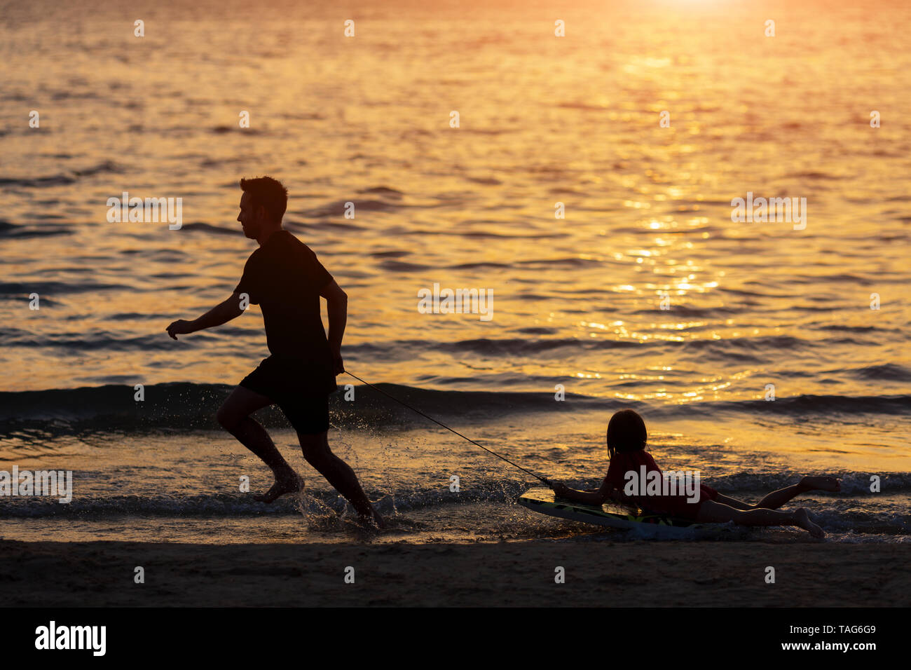 Silhouette padre e kid giocando sulla spiaggia al tramonto del tempo. Padre e kid avendo divertimento all'aperto Foto Stock