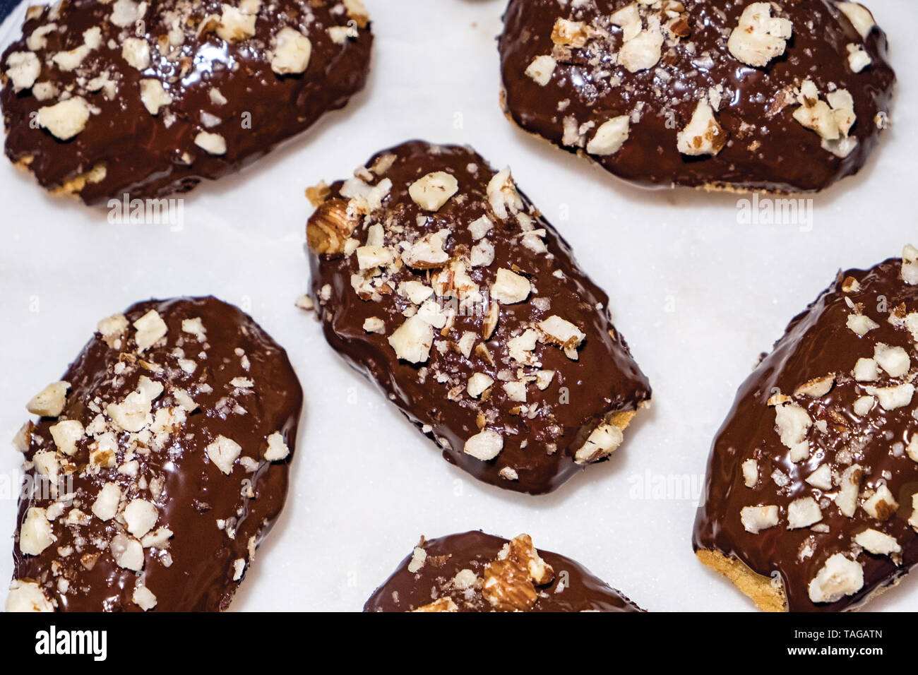 Vista superiore del francese Madeleines immersi nel cioccolato al latte con nocciole frantumate spruzzato sulla parte superiore, seduto su un marmo bianco sullo sfondo Foto Stock