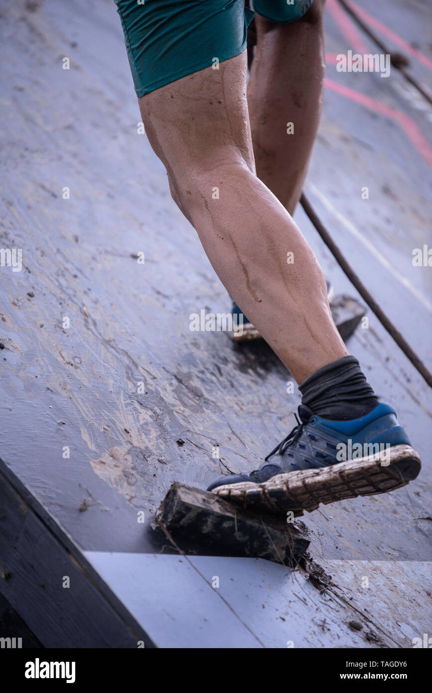 SOFIA, BULGARIA - 7 luglio 2018 - le gambe di un uomo che cerca di arrampicarsi su un sporco umido parete in legno per superare unil ostacolo corso di una gara di resistenza Foto Stock