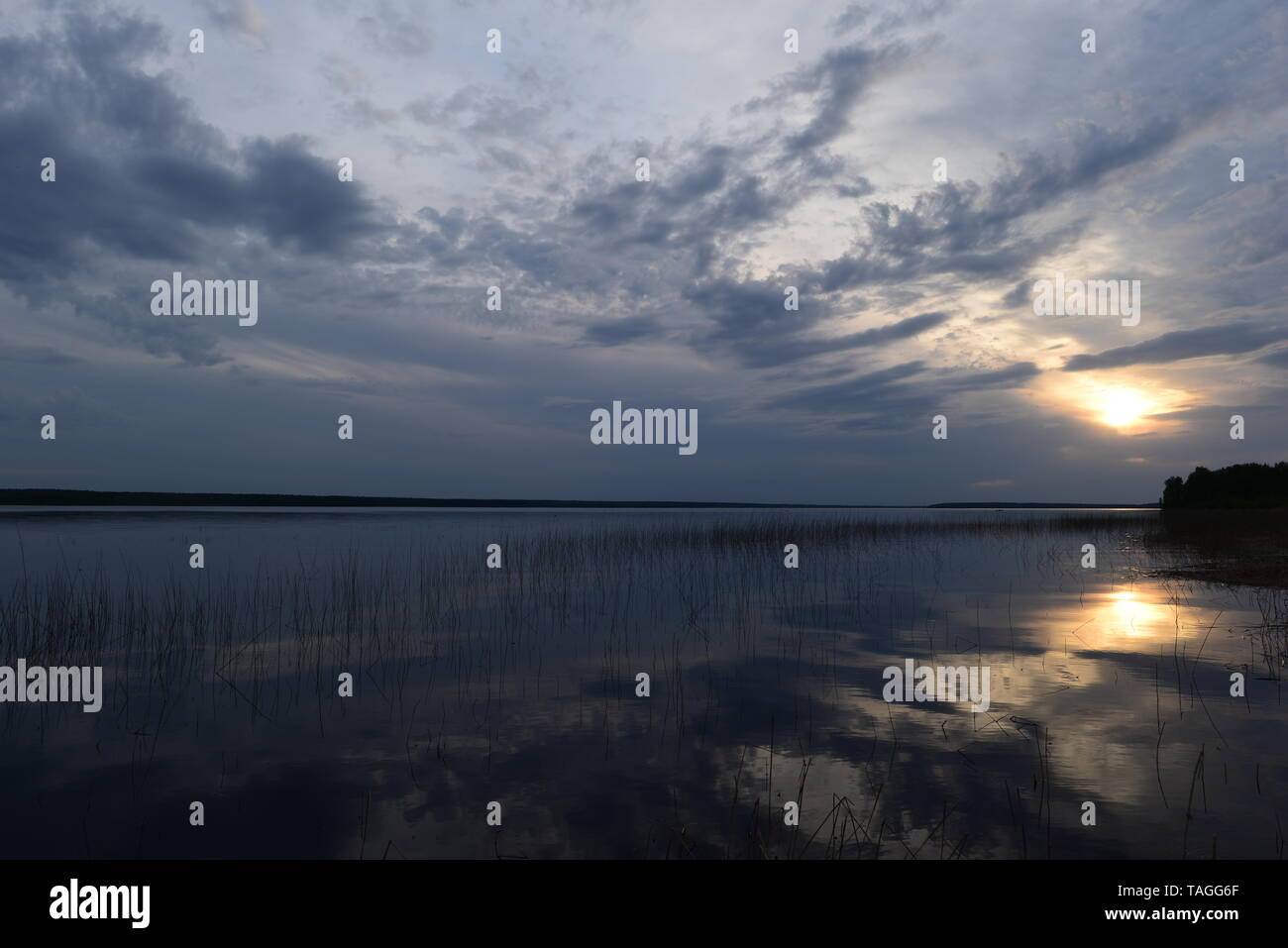 Cielo blu sulle nuvole nel bagliore luminoso del sole al tramonto con una riflessione sulla superficie dell'acqua del lago Foto Stock