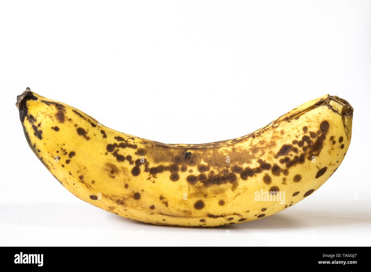 Un intero maturo banana giallo con macchie nere e lividi sulla sua buccia. Foto isolate in bianco. Foto Stock