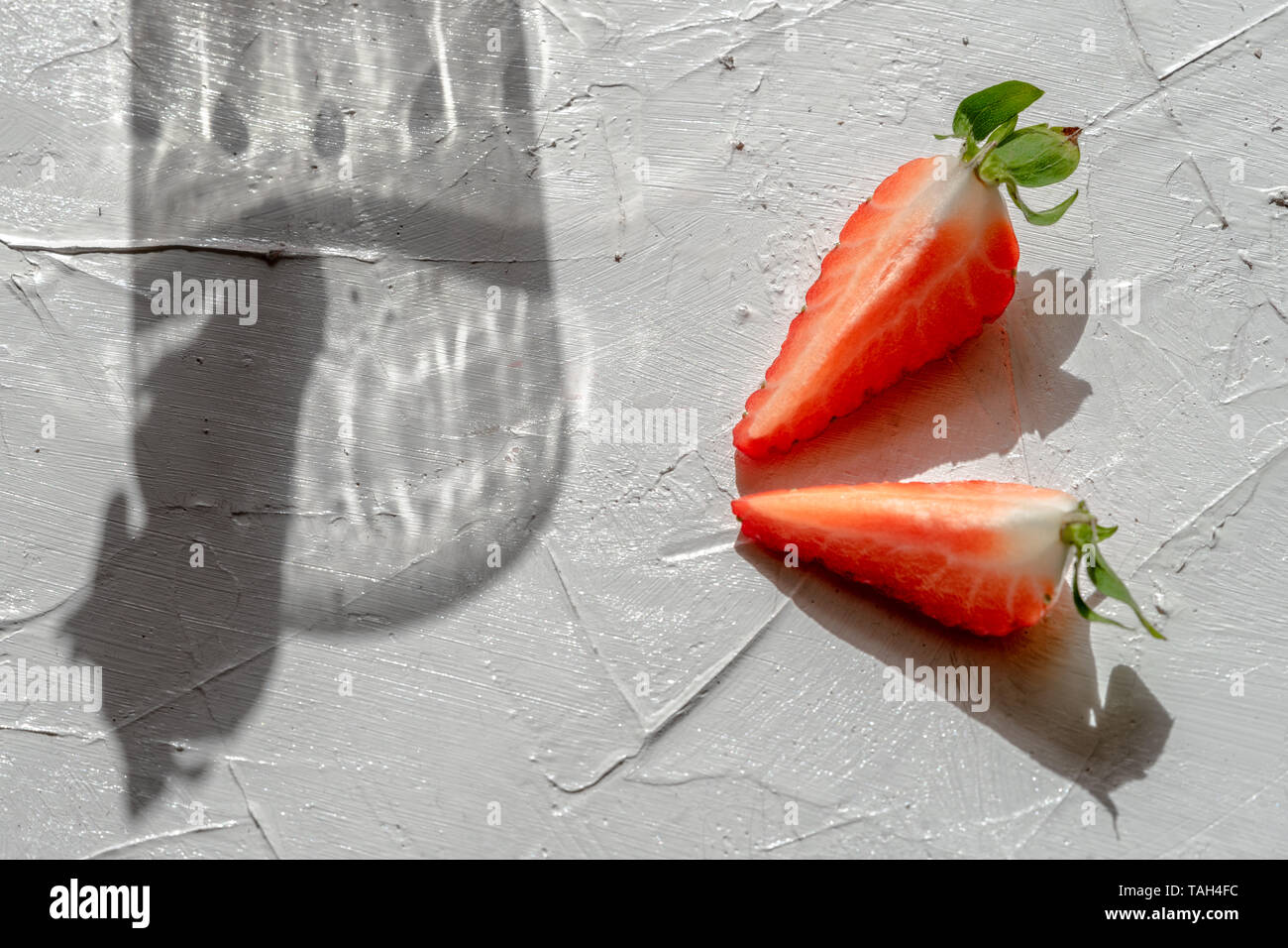 Gioco di ombre dal vetro e strawberrie su sfondo bianco Foto Stock