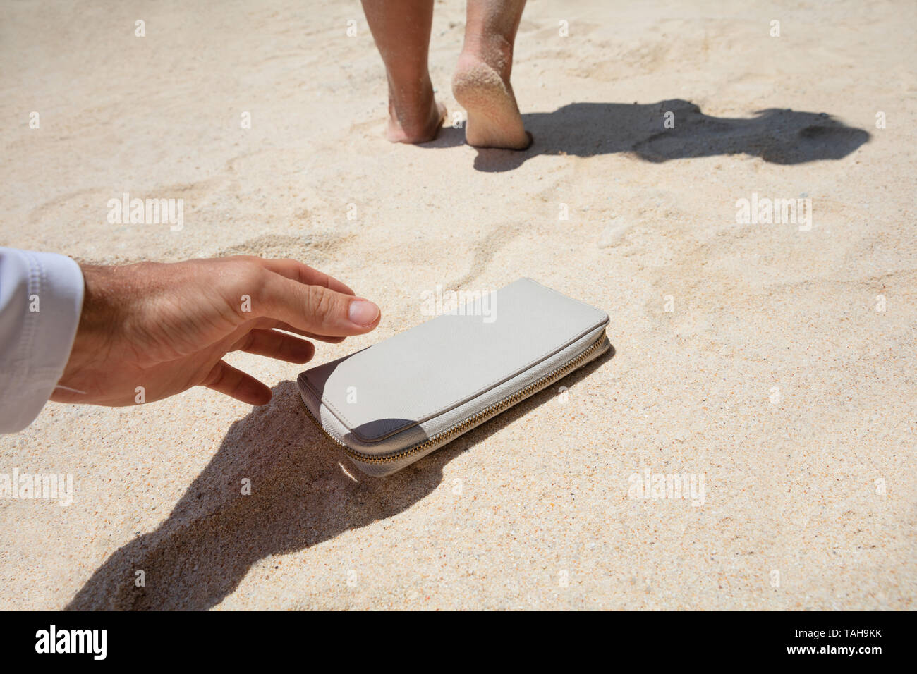 Close-up di un uomo prendendo donna portamonete perduto sulla sabbia in spiaggia Foto Stock
