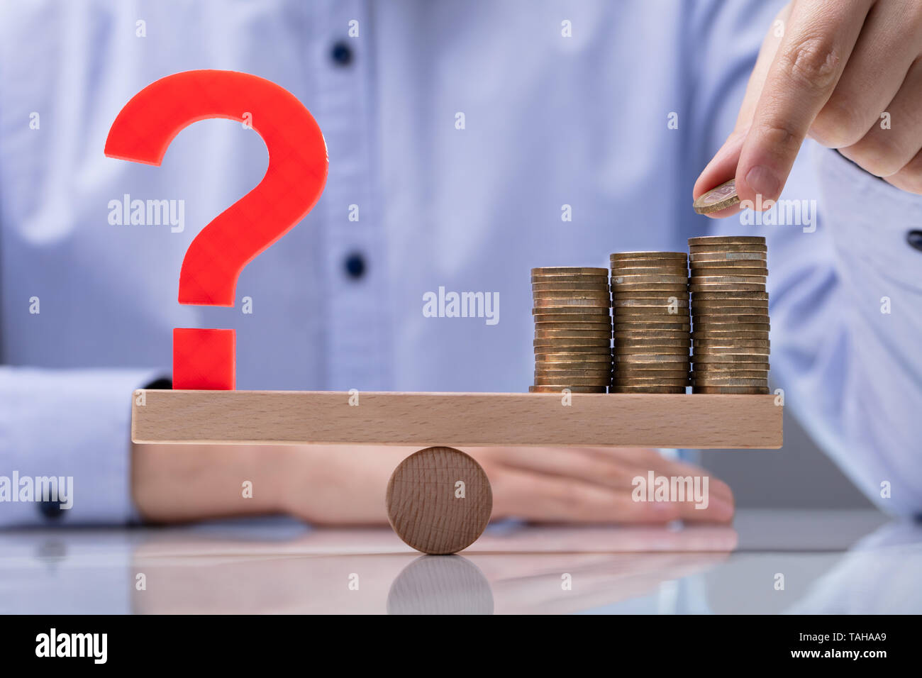 Ponendo mano moneta sulla sommità della pila di monete e punto interrogativo segno su altalena Foto Stock