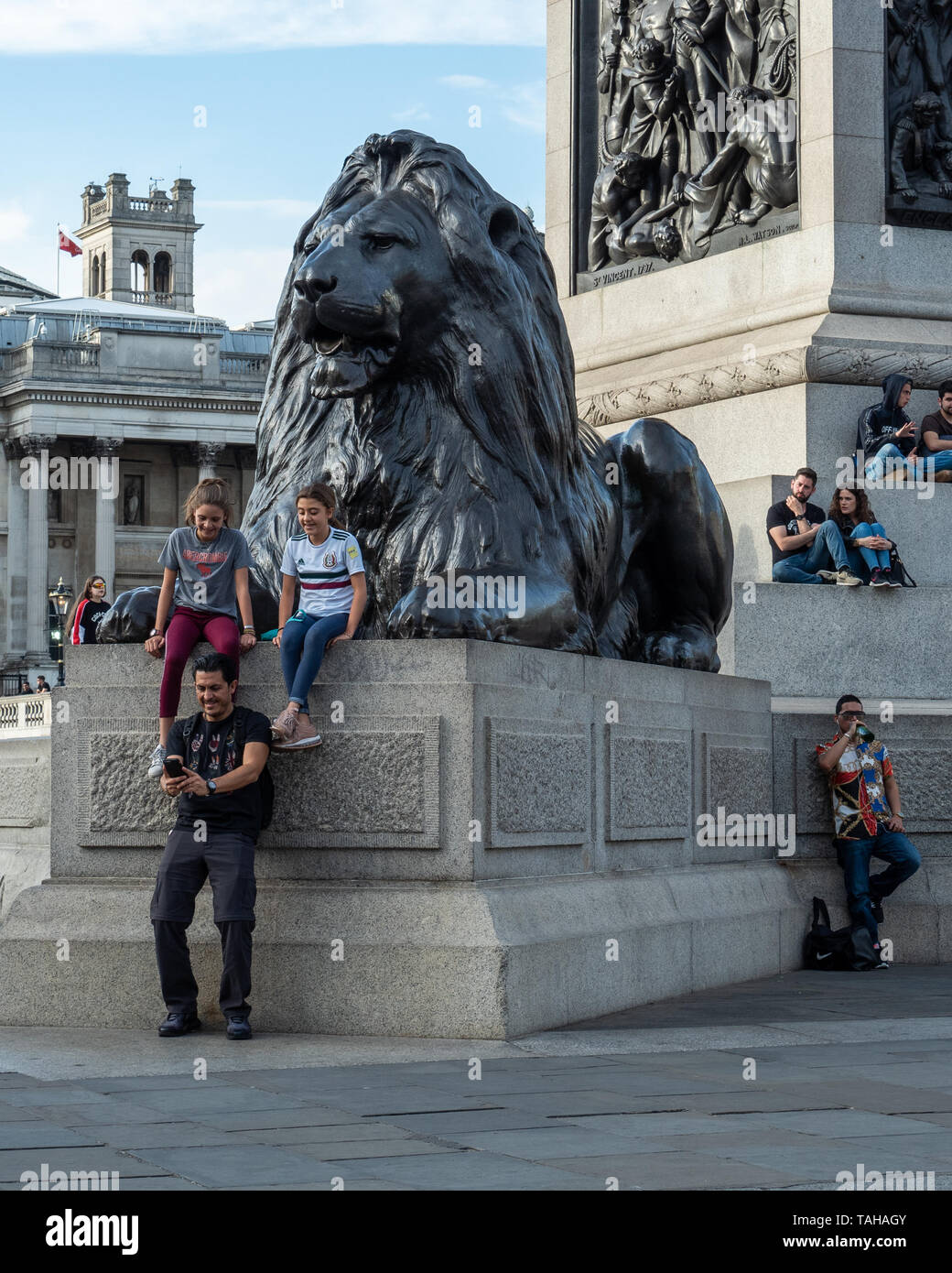 Le persone che si rilassano e si godono Trafalgar Square in una giornata di sole a Londra. Foto Stock