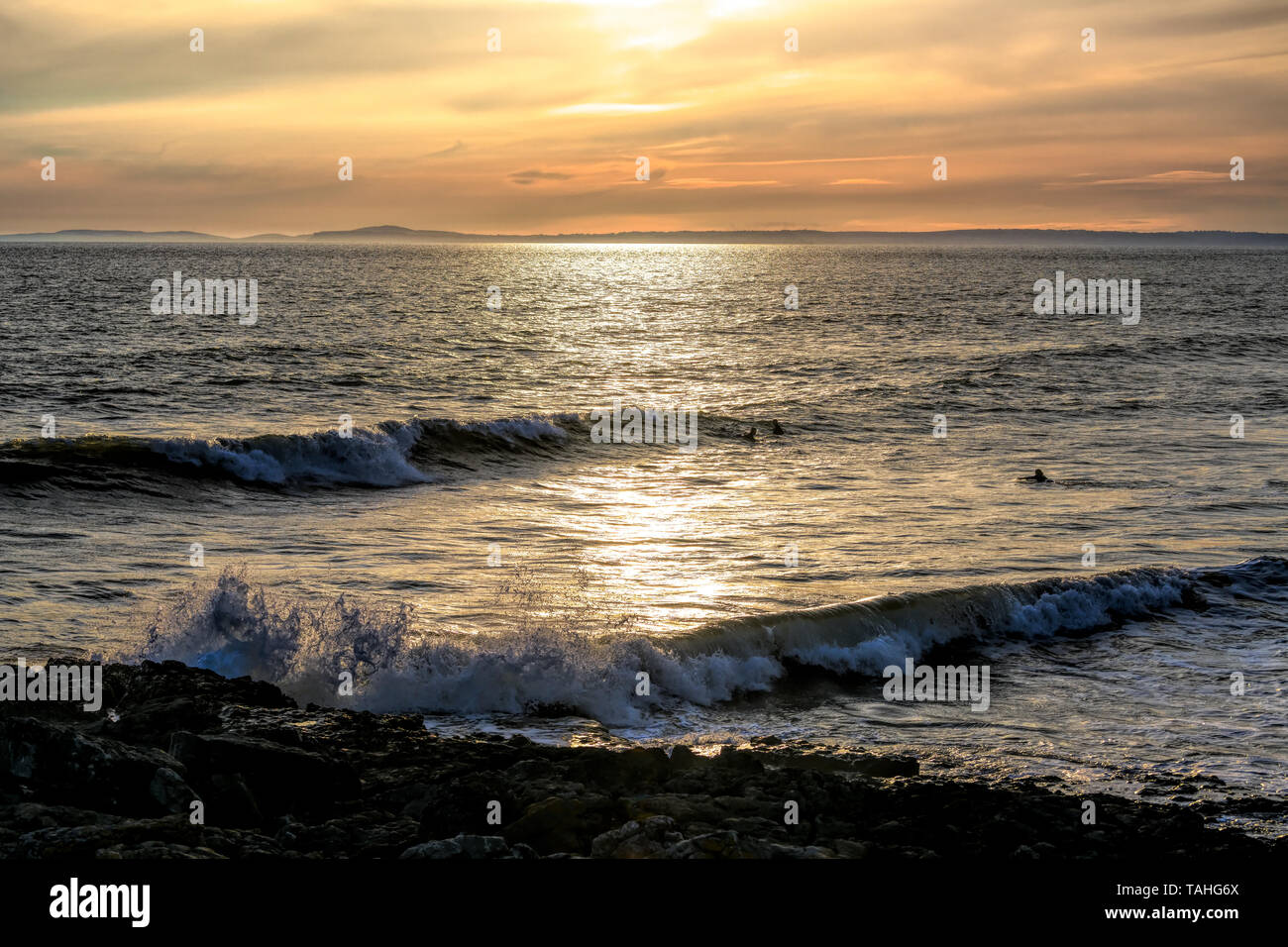 Tre Surfers Godetevi il tramonto come thet attendere awave, resto Bay Porthcawl, Regno Unito. Foto Stock
