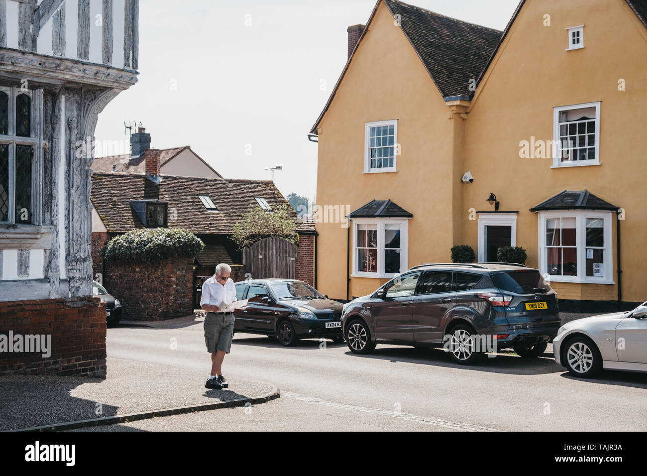 Lavenham, Regno Unito - 19 Aprile 2019: uomo in piedi e la lettura di una mappa nella parte anteriore del cottage colorati a Lavenham, un villaggio nel Suffolk, Inghilterra, famoso per Foto Stock