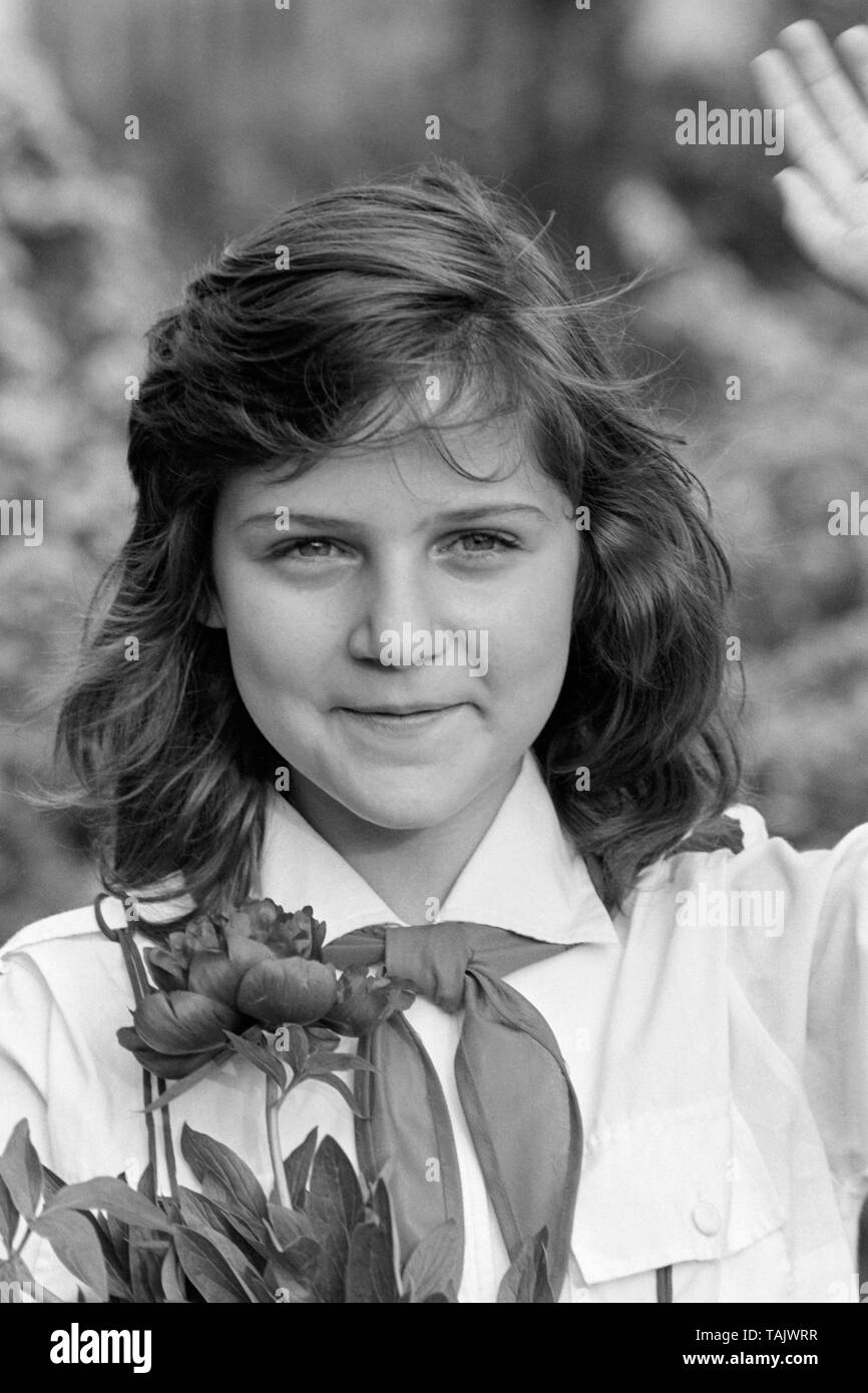 Giovani schoolgirl membro del movimento pioniere indossando la sua cravatta e uniforme tenendo un mazzo di fiori e salutando degli anni settanta Ungheria Foto Stock