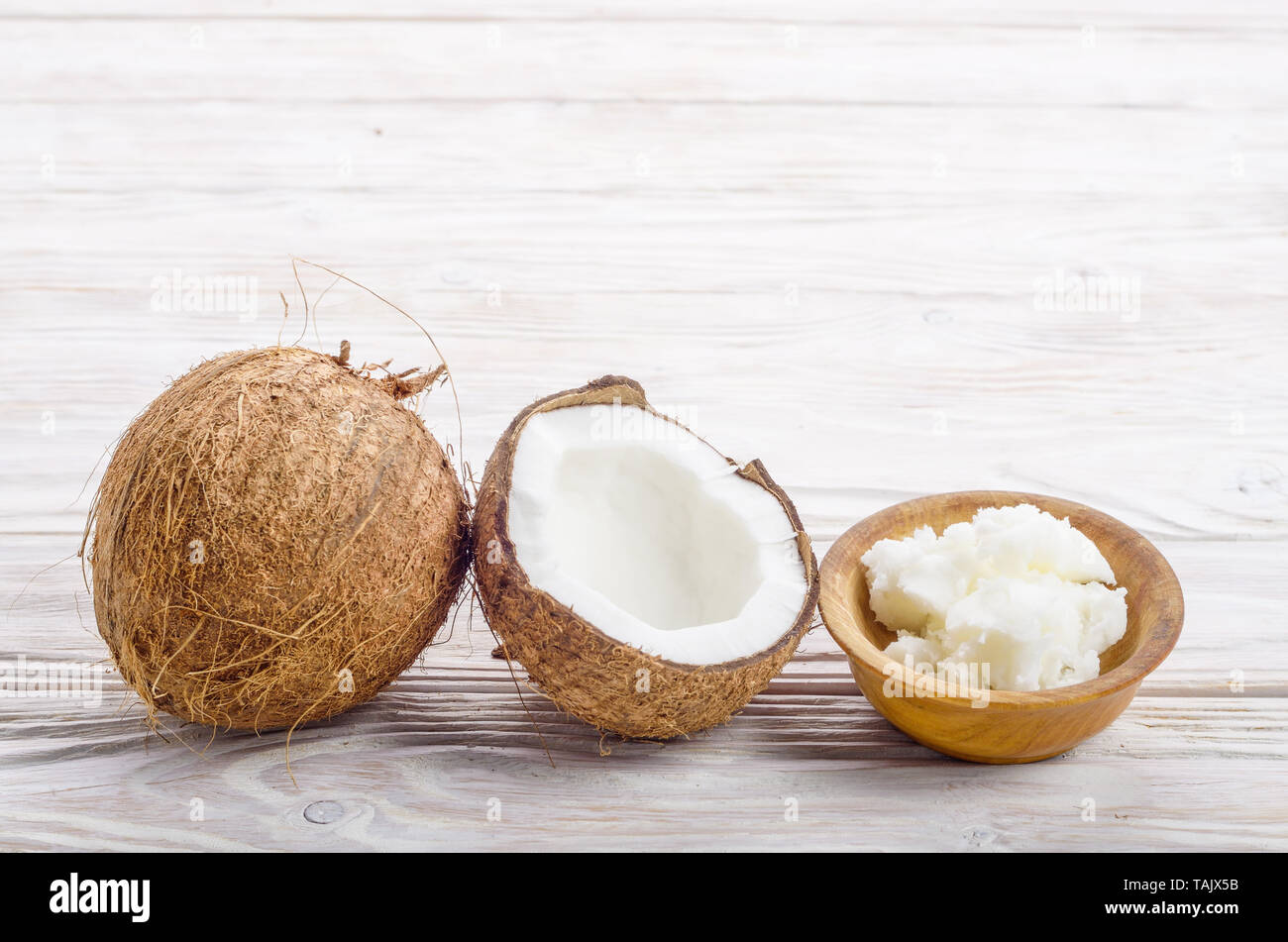 Sfondo di cocco, di guscio di noce di cocco, olio duro nella ciotola di legno bianco sul tavolo di legno Foto Stock