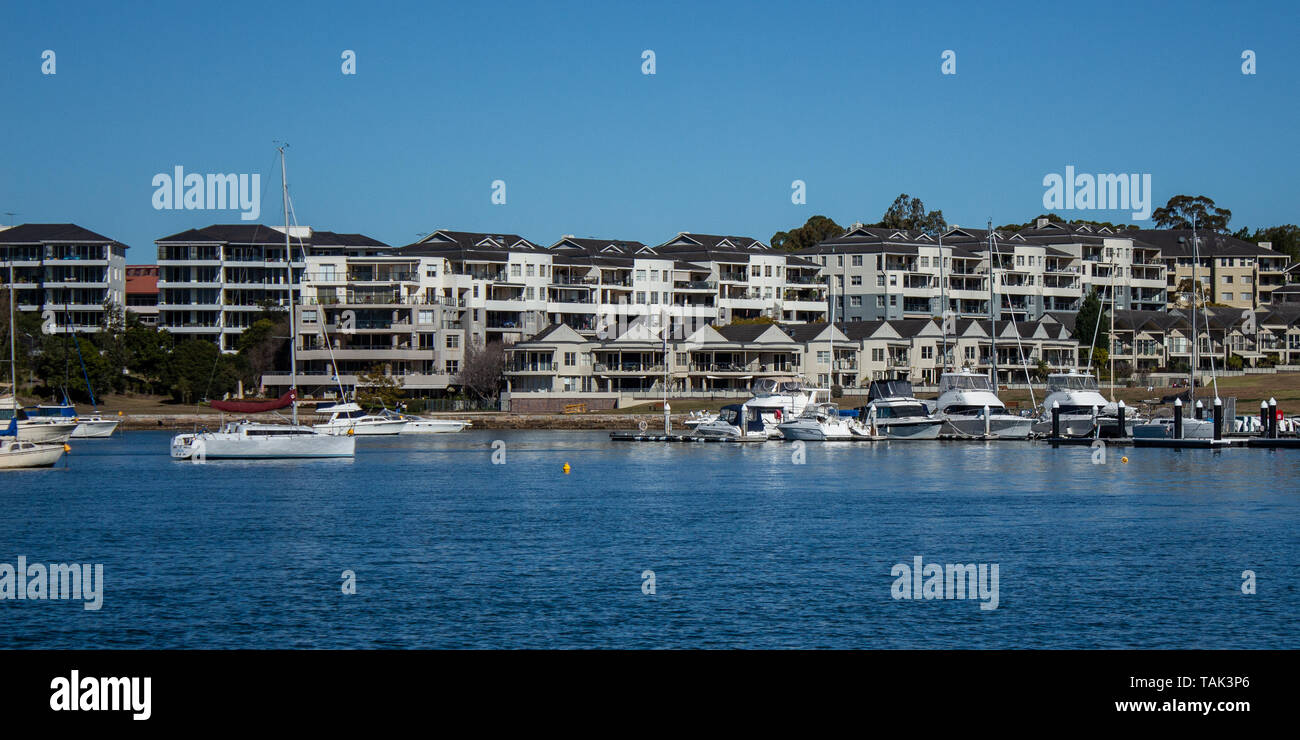 Harbourside appartamento condominio alloggiamento con barche galleggianti su acqua blu contro il cielo blu. Foto Stock