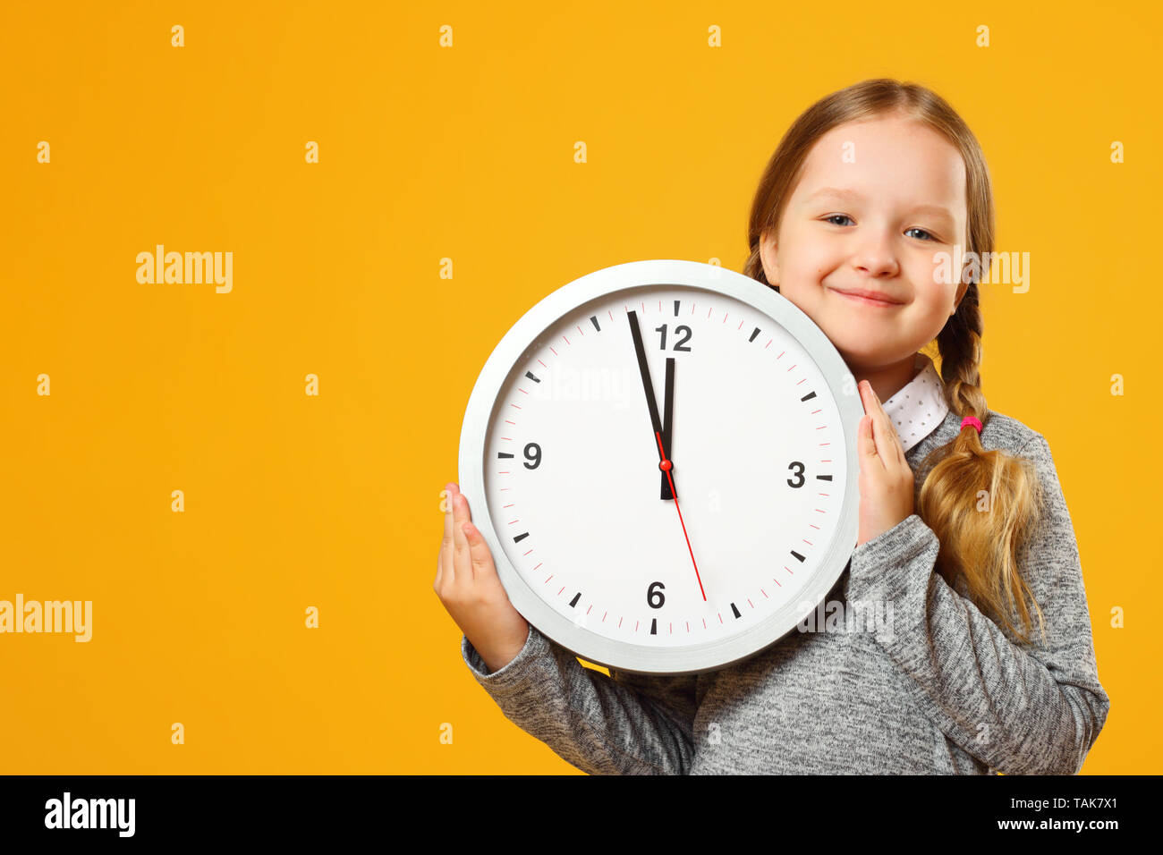 Bambina con pig-tail detiene un grande orologio su sfondo giallo. Il concetto di educazione, la scuola, la temporizzazione, il tempo per imparare. Primo piano verticale. Copia sp Foto Stock