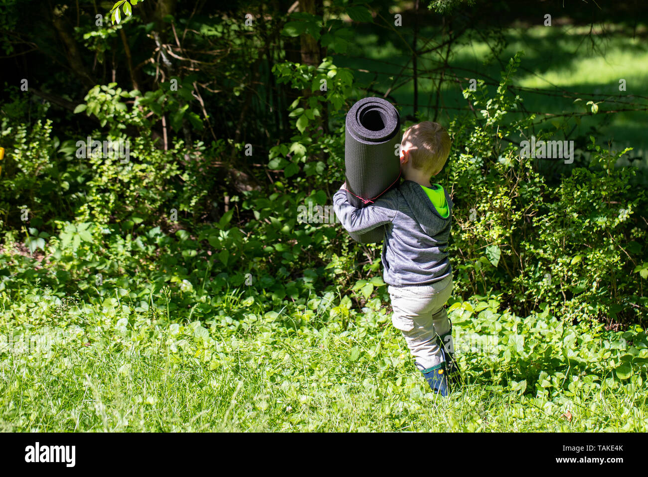 Bimbi maschio porta arrotolato mat attraverso l'erba. Foto Stock