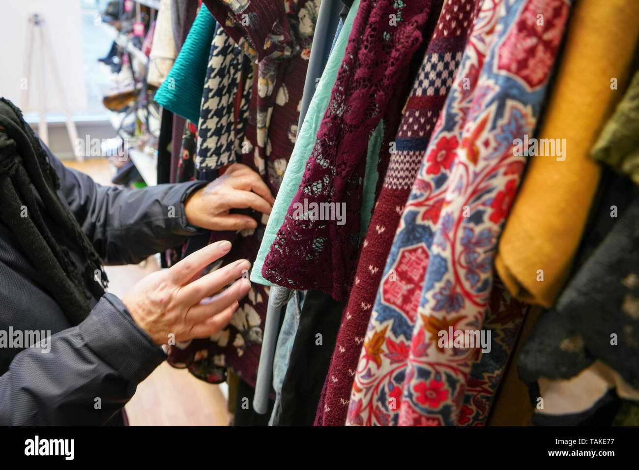 Senior donna passando attraverso i vestiti di seconda mano la parsimonia carità shop, dettaglio sul suo muovendo le mani. Foto Stock