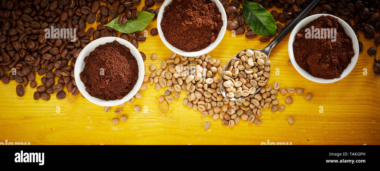 Specialty Coffee panorama banner con un assortimento di arrosti e i fagioli crudi sparsi in legno di colore giallo con tre tazze di caffè appena macinato e verde lea Foto Stock