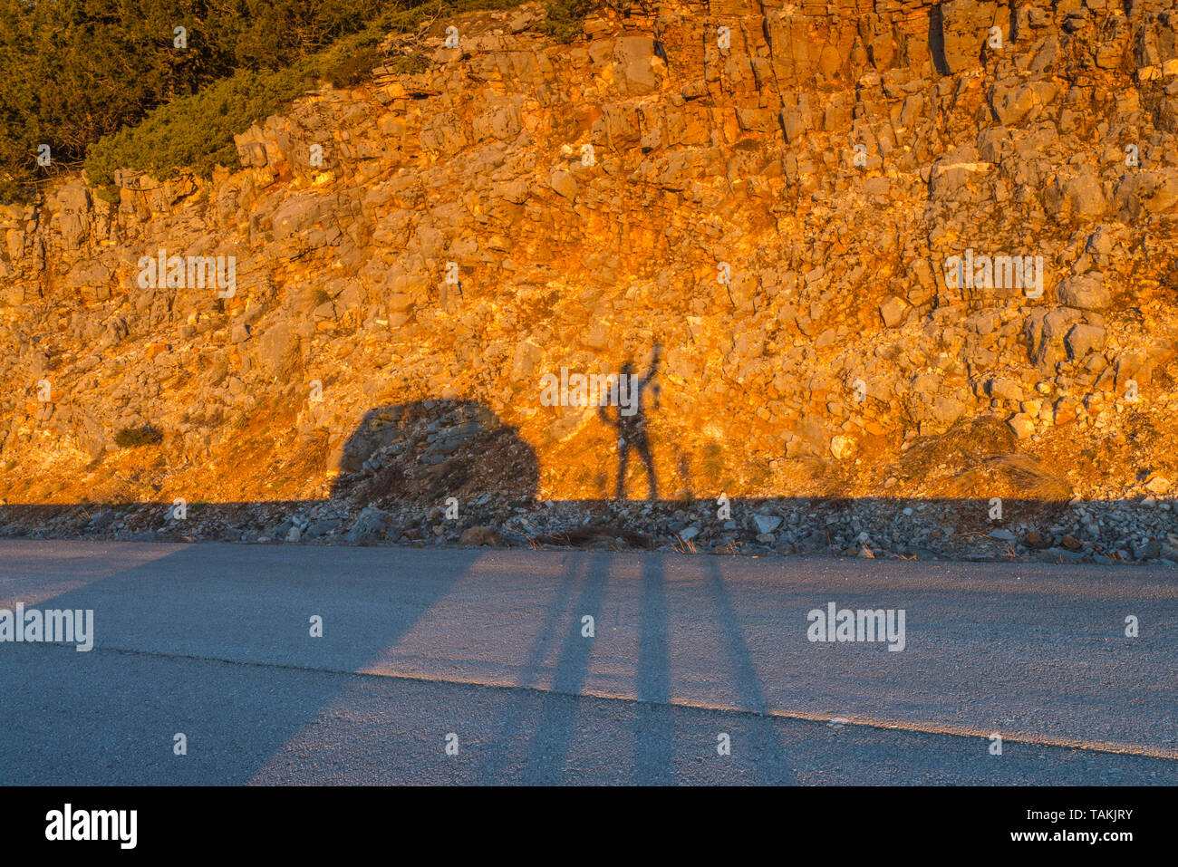 Un viaggiatore a giocare con la sua ombra al sorgere del sole lungo la strada. Ombra di una persona colata su una golden parete di roccia. Foto Stock