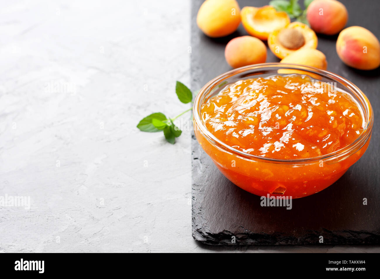 Confettura di albicocche in una ciotola di vetro, fresche Albicocche su un calcestruzzo di colore grigio sullo sfondo di close-up Foto Stock