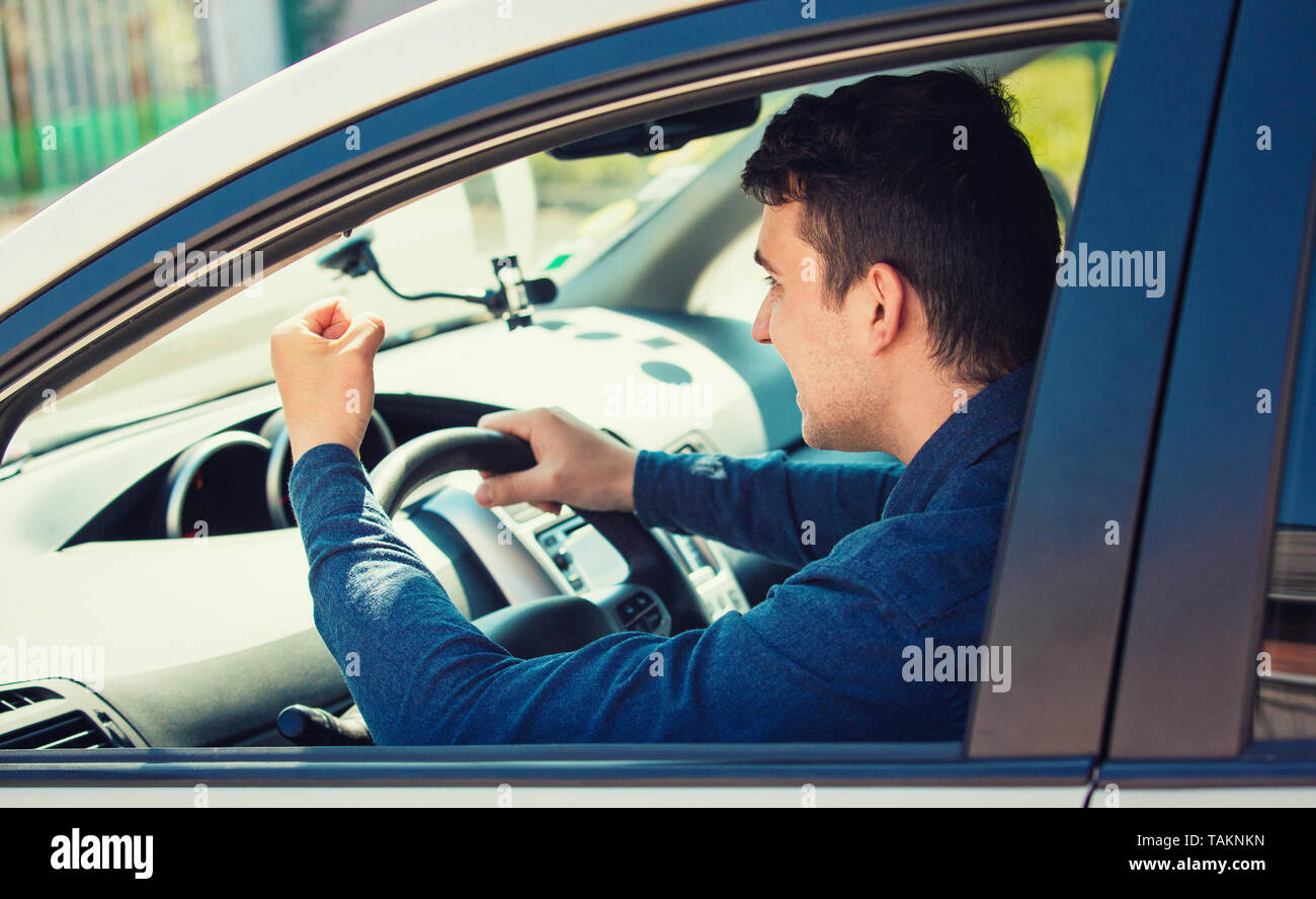 Giovane conducente urlando e agitando il pugno minaccia un altro automobilista. Infastiditi e arrabbiato ragazzo gridando e urlando in sua automobile. Cattivo e aggressivo Foto Stock