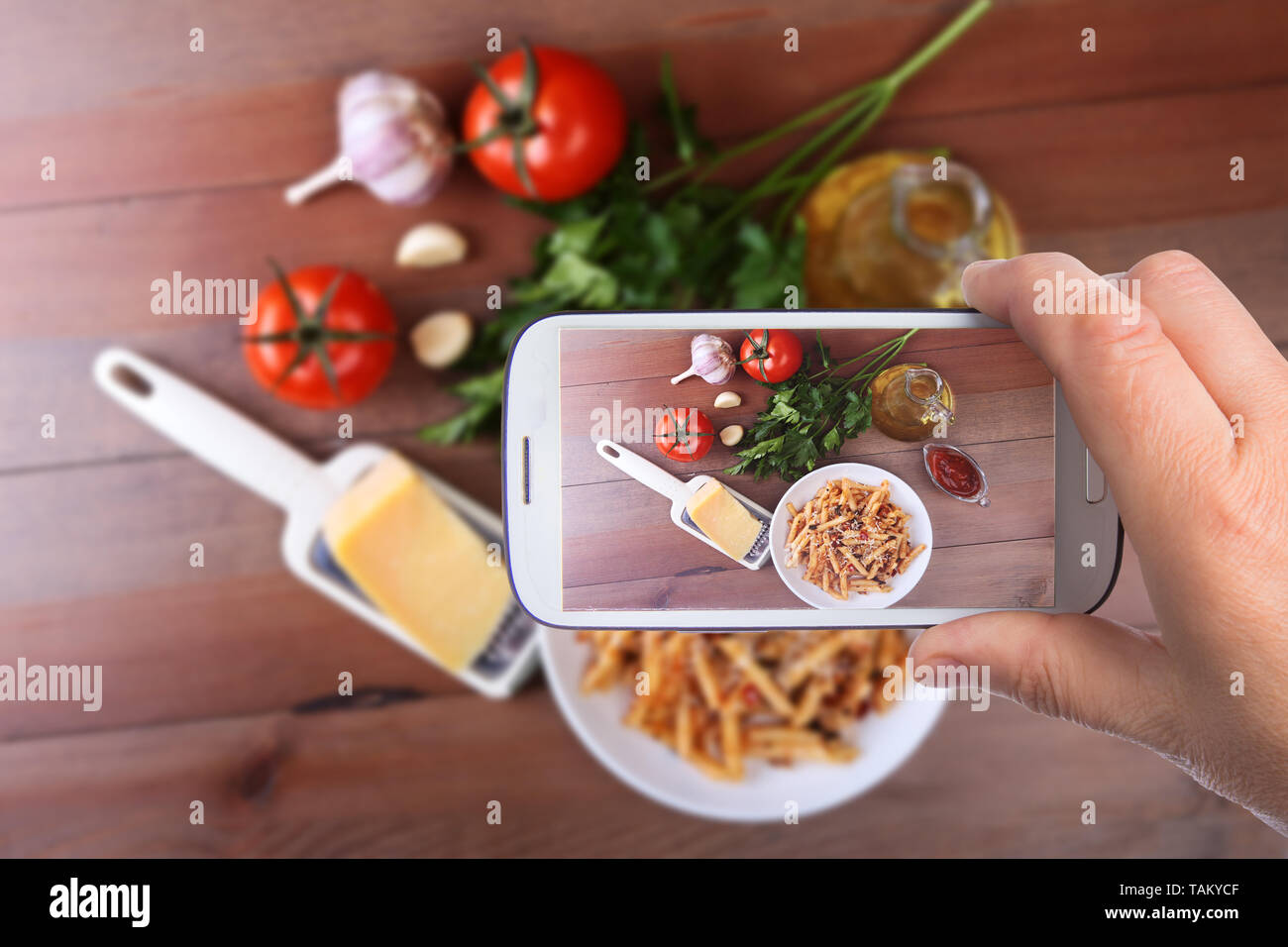 Le mani di uomo con lo smartphone tenendo foto penne piccante pasta bolognese con verdure, peperoncino e formaggio in salsa di pomodoro sullo sfondo di pomodori Foto Stock