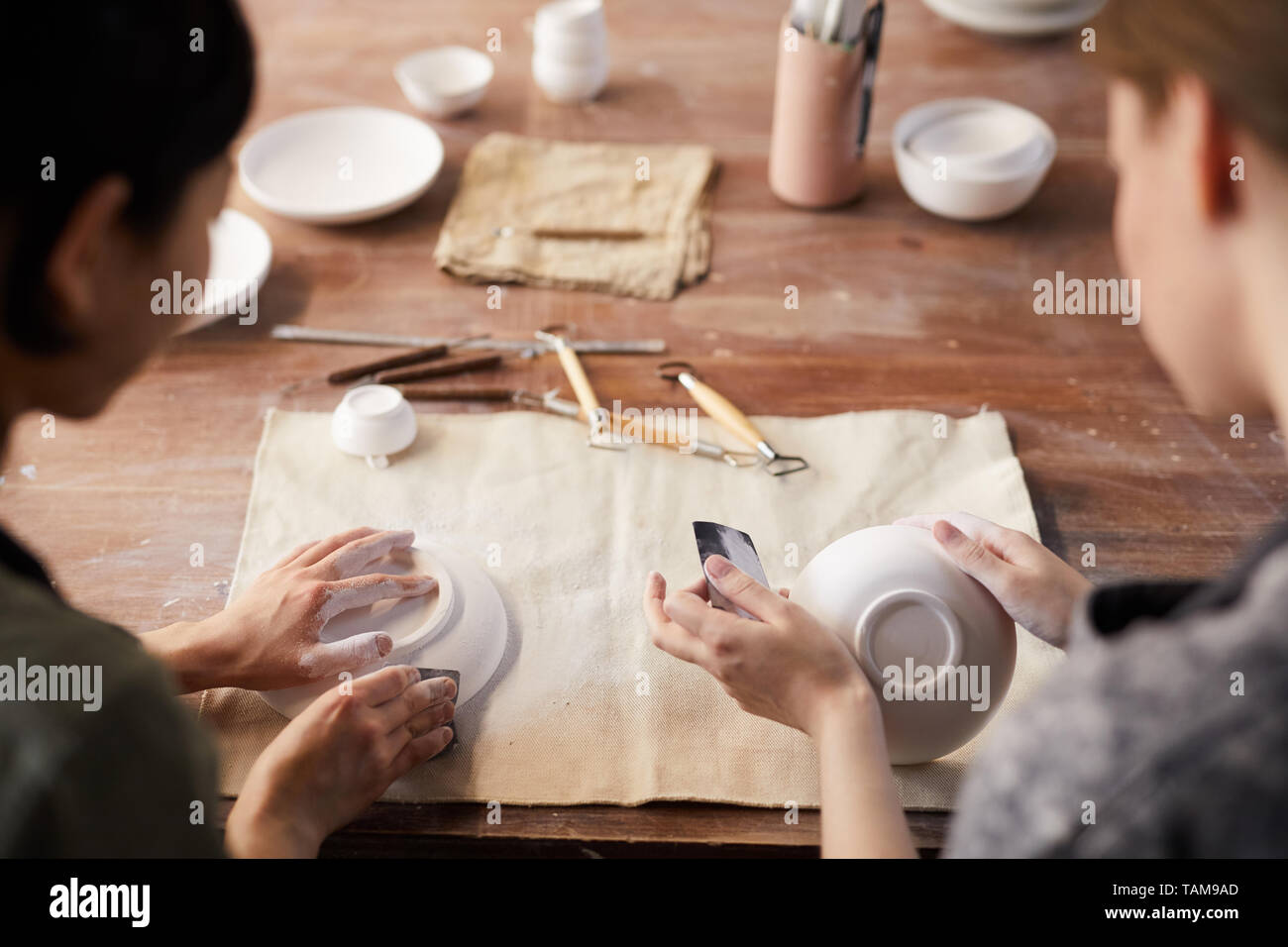 Vista posteriore di un irriconoscibile artigiane seduti al vecchio tavolo in legno e lucidatura di piatti a base di argilla con sandpapers in officina Foto Stock